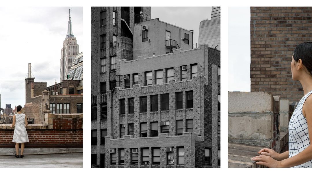 Woman in dress overlooks cityscape with Empire State Building. Rooftop setting with aged brick. Architectural study in monochrome.