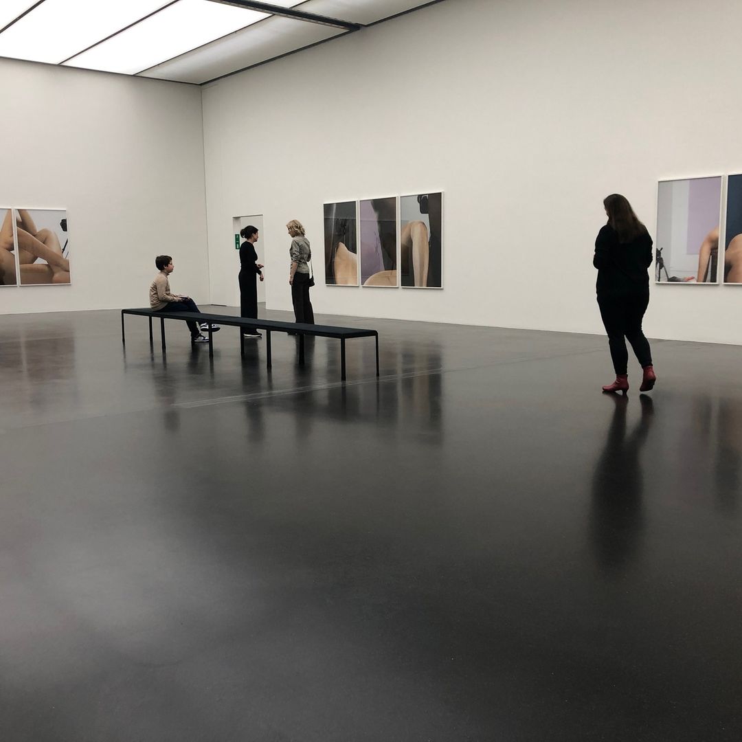 People at a modern art museum, viewing framed photographs. A child sits on a bench in the gallery, with shiny black floors and bright lights.