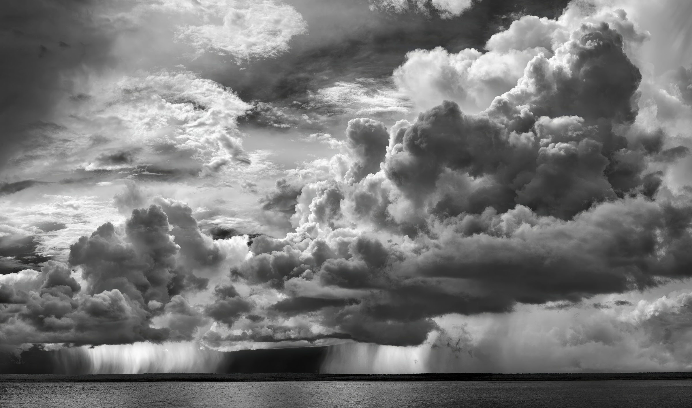Monochrome seascape featuring dark storm clouds filling the sky above calm water, punctuated by rain shafts in a horizontal composition.
