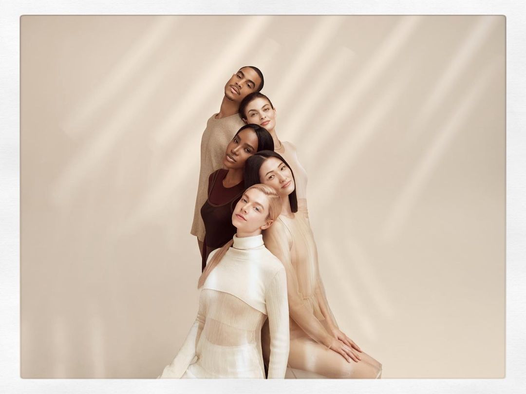 Group portrait of five diverse adult models in a neutral-toned photo studio with soft window light, wearing beige and brown clothing.