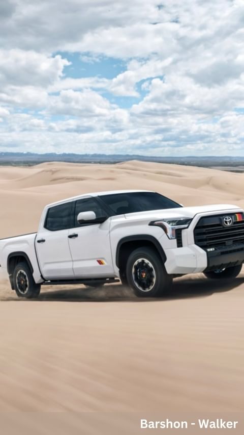 A white four-door Toyota Tundra pickup truck on a desert dune under a blue sky with clouds and sand dunes in the background.