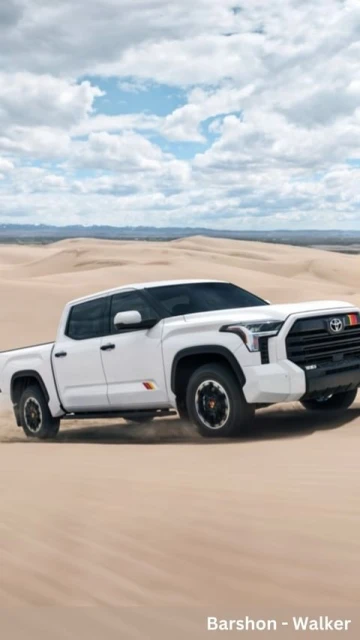 A white four-door Toyota Tundra pickup truck on a desert dune under a blue sky with clouds and sand dunes in the background.