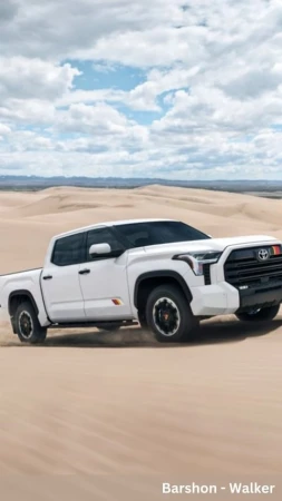 A white four-door Toyota Tundra pickup truck on a desert dune under a blue sky with clouds and sand dunes in the background.