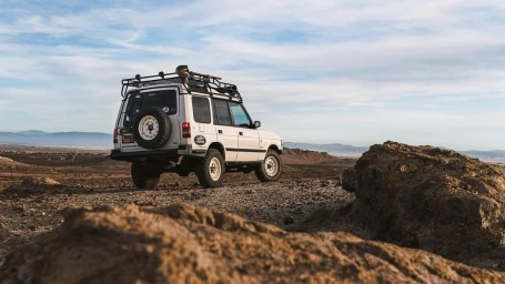 White Land Rover Discovery off-road vehicle parked on a rocky desert landscape under a blue sky.