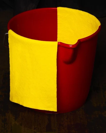 A red plastic bucket has a yellow cloth hanging from its side in a high-contrast studio shot, emphasizing color and texture.