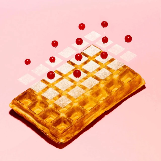 Overhead shot of a waffle topped with powdered sugar and red currants on a pink background with patterned diamond shadows.
