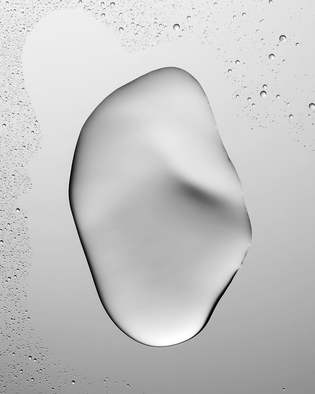 Abstract close-up of a clear liquid drop on a gradient gray surface with smaller droplets in the background, creating a clean, minimal image.