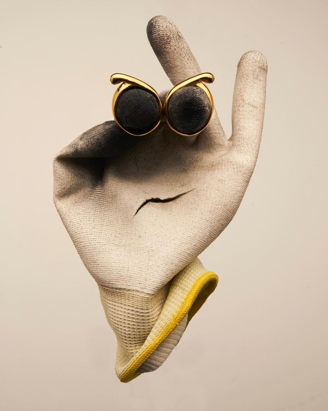 A surreal studio shot of a used work glove with an owl-eye accessory attached, set against a neutral background with creative presentation.