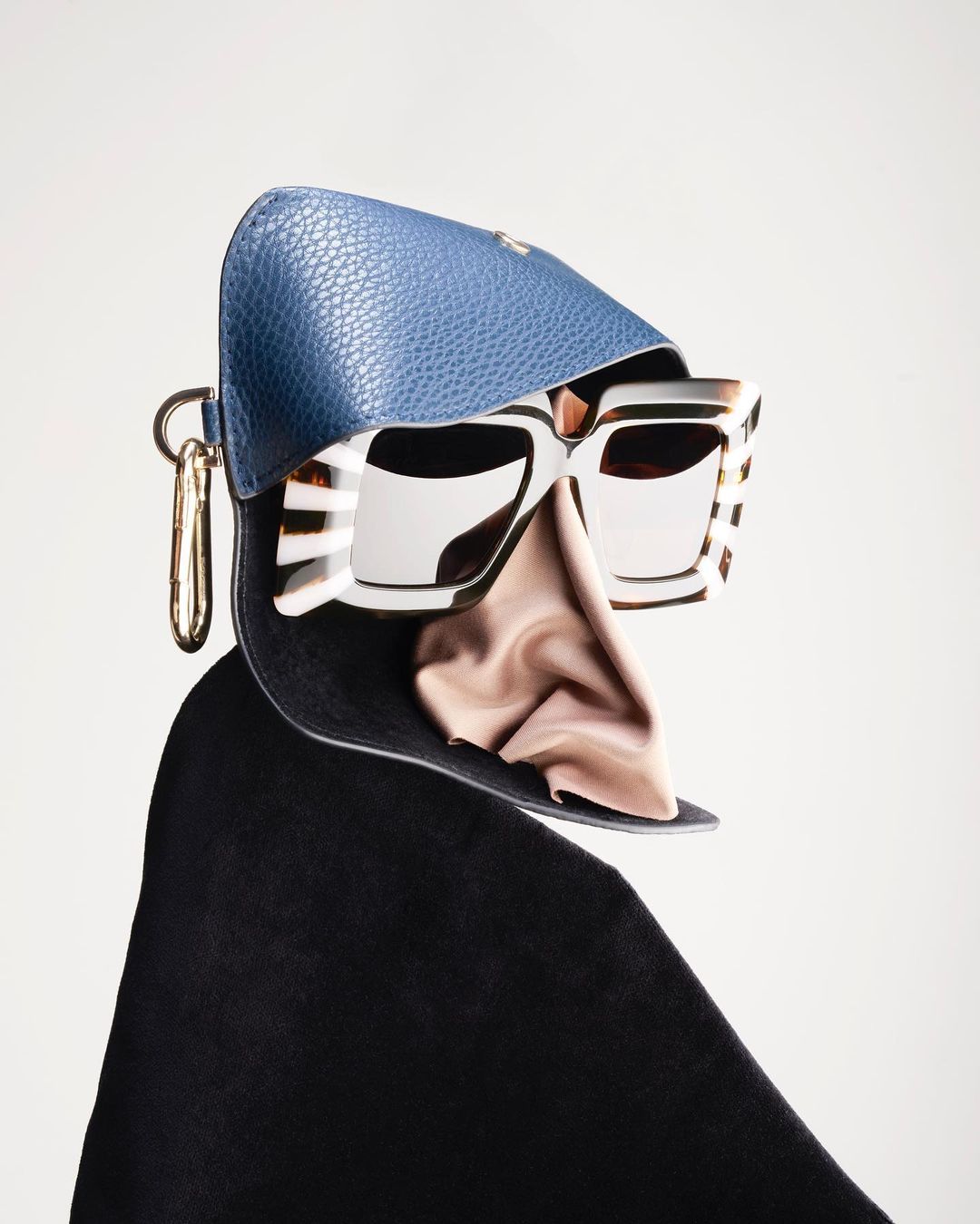 Still life shot of open blue leather glasses case featuring white sunglasses with gold accents and pink silky cloth on light background.