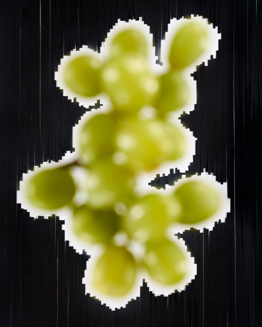 Overhead shot of a blurry, abstract-style image of a bunch of green grapes on a black background with vertical lines.