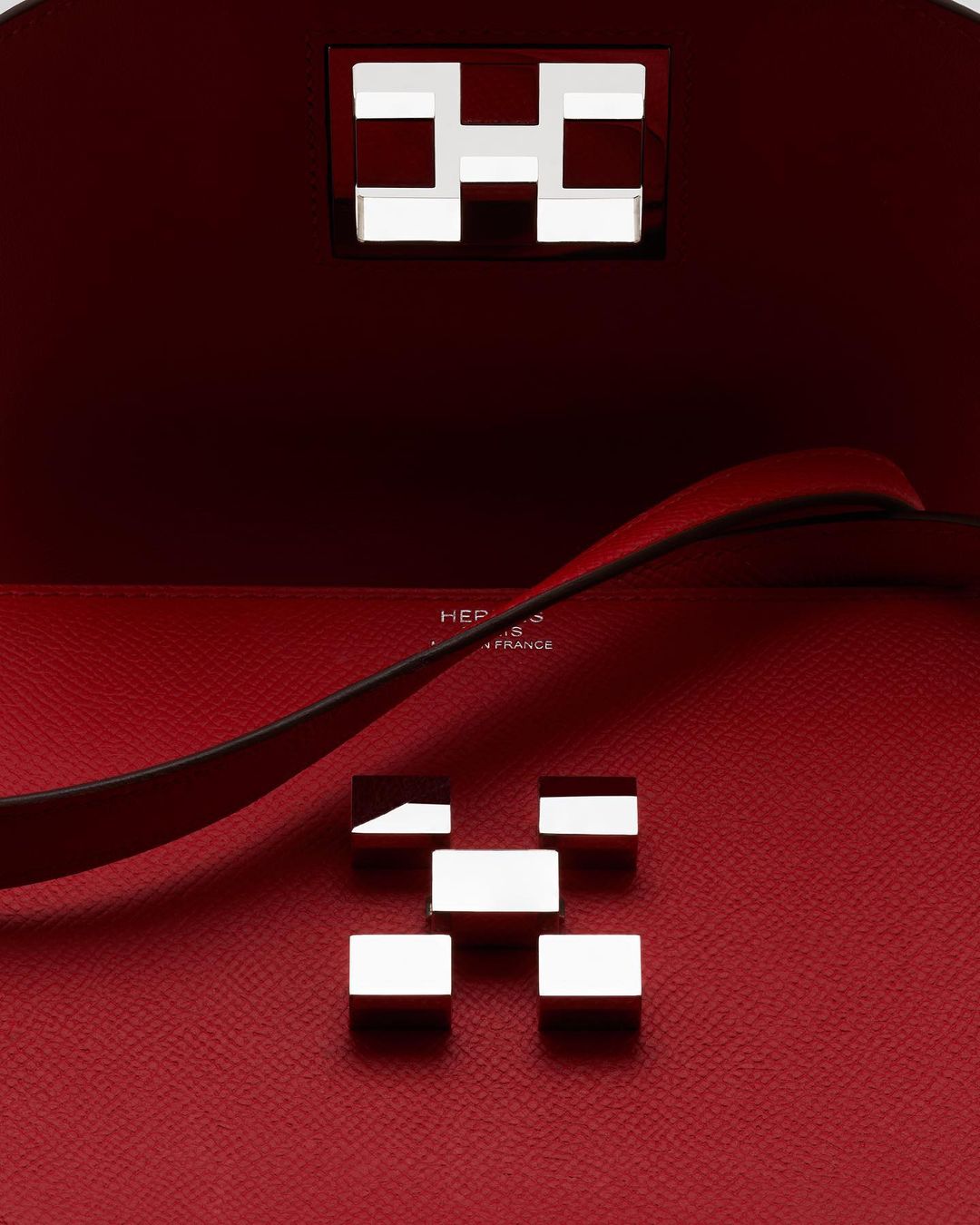 Close-up of a red leather handbag interior with silver metal hardware forming an 'H' design, showcasing luxury fashion and craftsmanship.