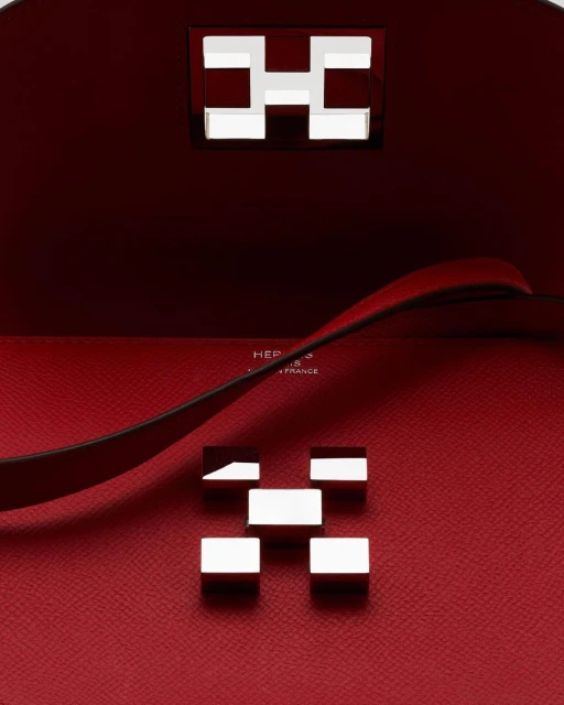 Close-up of a red leather handbag interior with silver metal hardware forming an 'H' design, showcasing luxury fashion and craftsmanship.