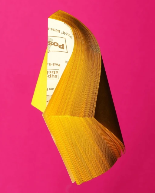 Stack of yellow Post-it notes on pink background. Office supply still life. Stationery product shot, bright and saturated.