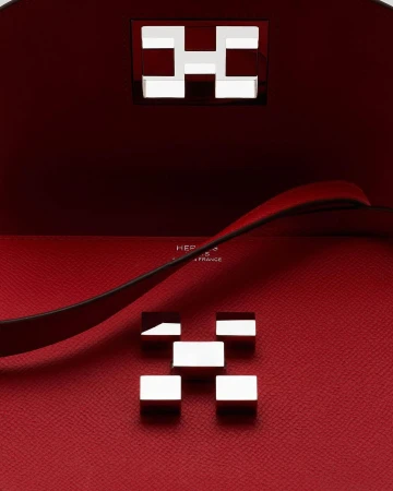 Close-up of an Hermès handbag interior featuring a red leather lining and two silver metal 'H' logo hardware pieces.