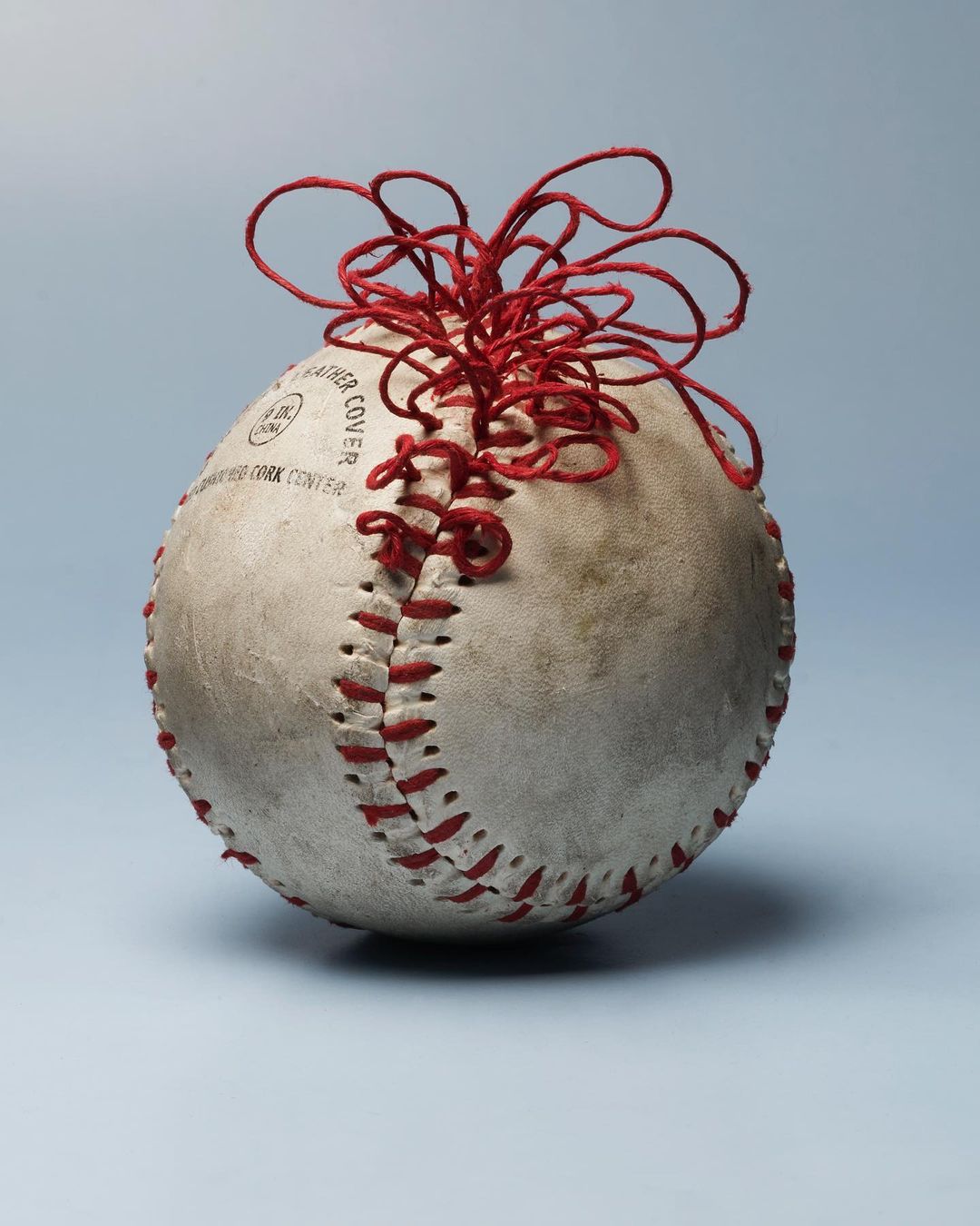 Close-up of a vintage baseball with red stitches and twine against a soft blue backdrop, creating a striking sports art image.