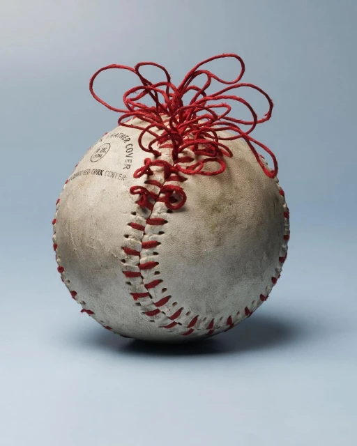 Close-up of a vintage baseball with red stitches and twine against a soft blue backdrop, creating a striking sports art image.