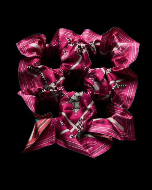 Close-up of a pink scrunchie made from patterned silk fabric against a solid black background in a studio setting with controlled lighting.