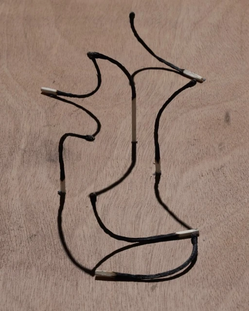 Burnt matchsticks arranged in an abstract shape against a light brown wooden surface, creating a visually striking contrast.