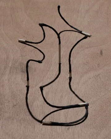 Burnt matchsticks arranged in an abstract shape against a light brown wooden surface, creating a visually striking contrast.
