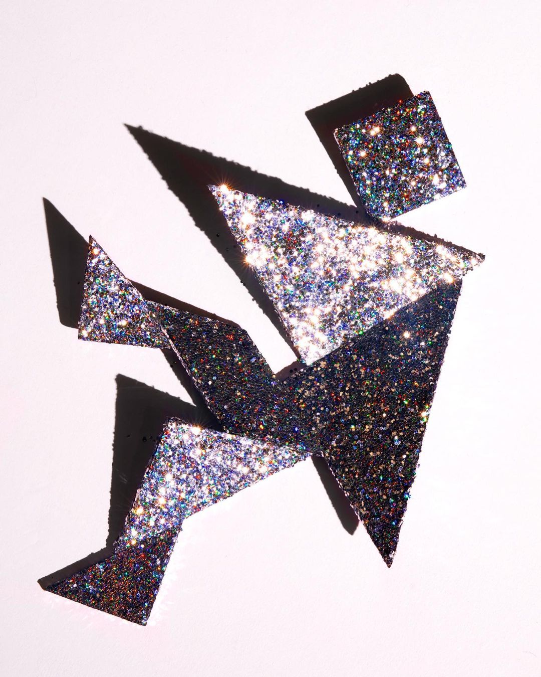 Abstract art installation with glittery geometric shapes and shadows on white background, creating a sparkling, dynamic visual composition.