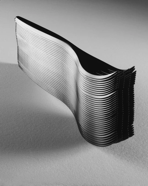 Stack of black and white, undulating, horizontally-aligned paper forming an abstract shape against a grey gradient background.