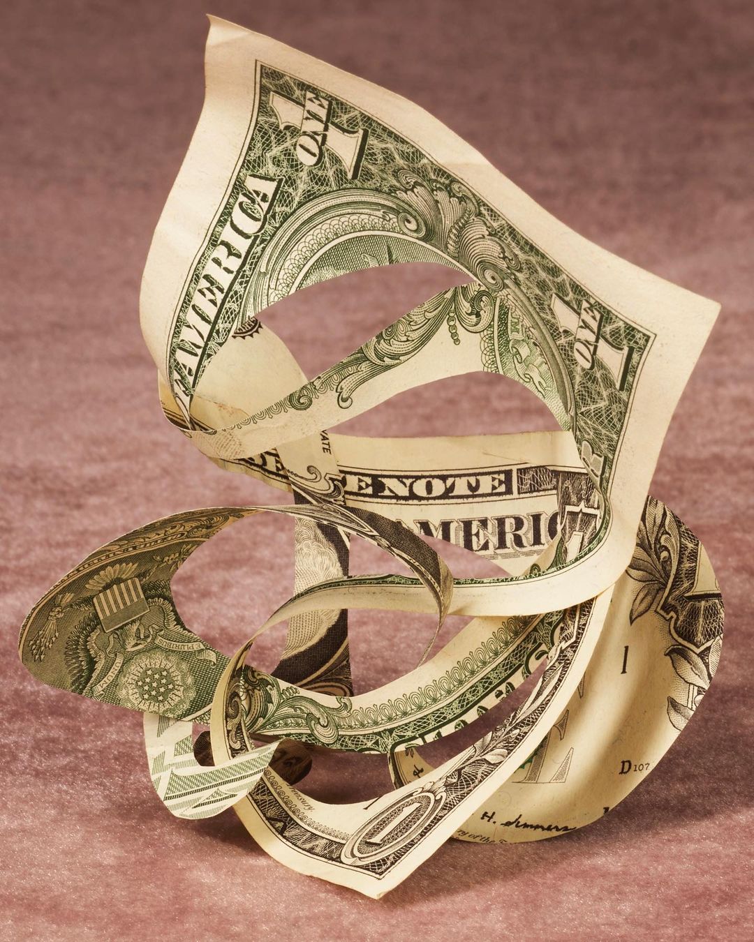 Close-up abstract still life shot of a gently twisted US one dollar bill against a pink textured background in soft studio lighting.