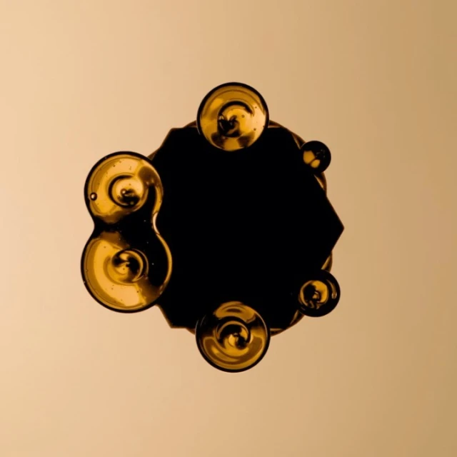 Abstract art featuring golden orbs surrounding a dark, geometric shape against a muted gold backdrop, creating a captivating visual composition.