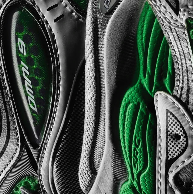 Close-up detail of a grey and green athletic shoe showing the textures, patterns, and construction of the footwear.