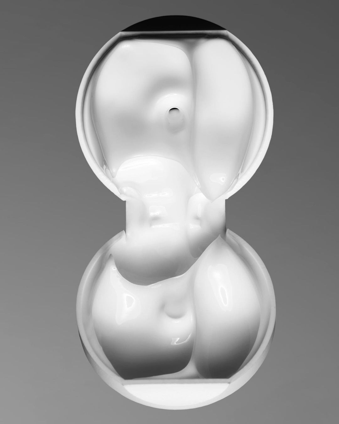 Abstract photography of two interconnected, clear glass spheres with internal distortions, set against a neutral gray backdrop.