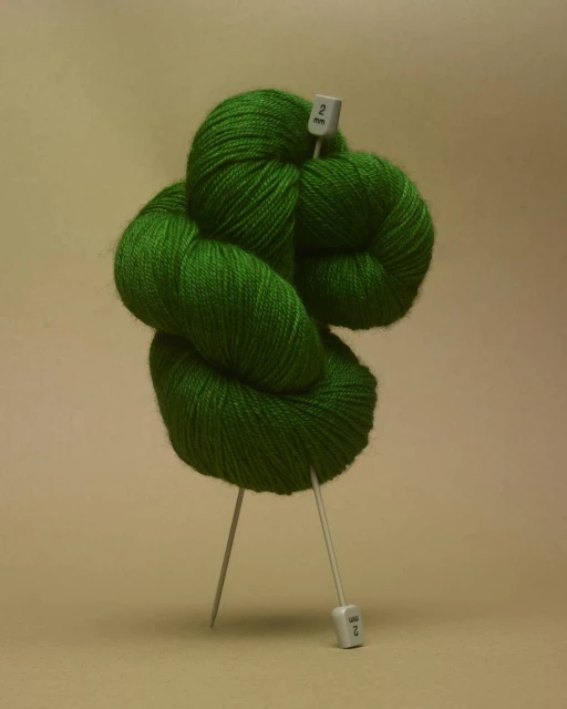Still life shot of a bright green ball of yarn with knitting needles, creating a minimalist and colorful composition.