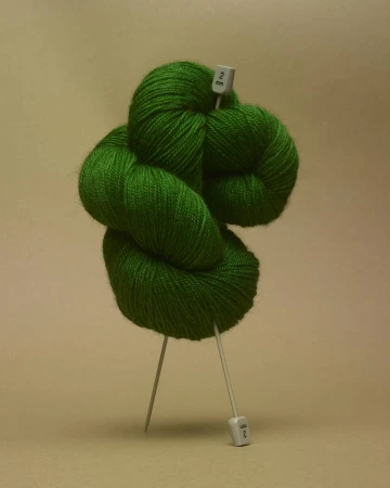 Still life shot of a bright green ball of yarn with knitting needles, creating a minimalist and colorful composition.