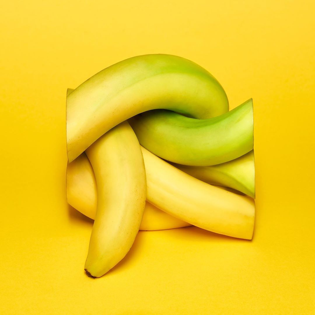 Cluster of yellow and green bananas interwoven on a solid yellow background, creating a visually striking and appetizing still life.
