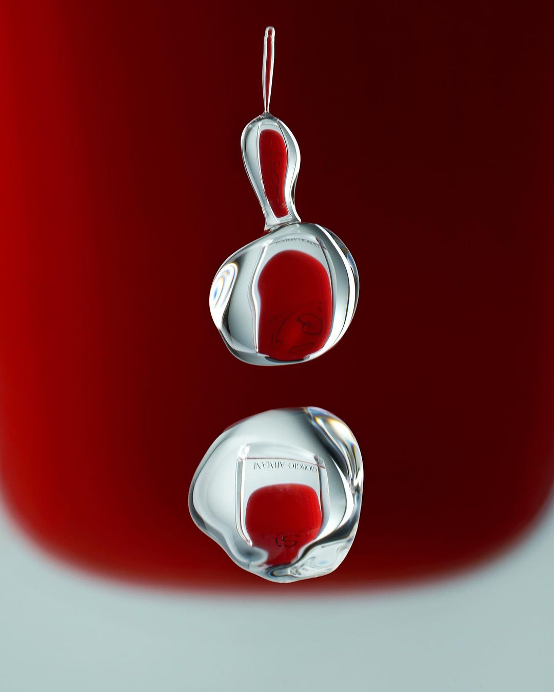 Macro studio shot: two abstract drops of reflective liquid suspended in the air, showing a red background and logo reflection.