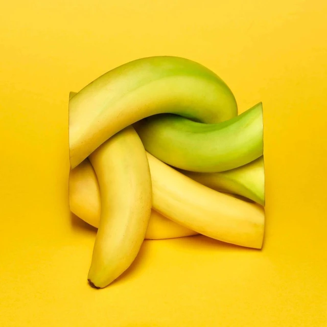 Vibrant still life of interlaced yellow and green bananas against a solid yellow background, ideal for food or healthy lifestyle themes.