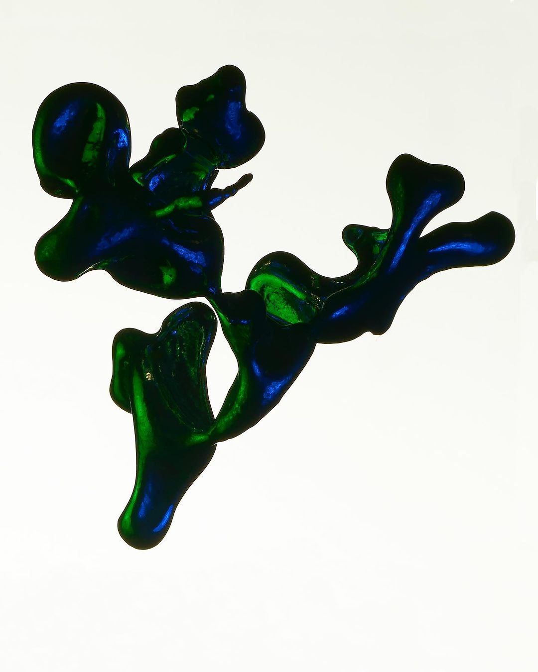 Abstract blue and green glossy ink blotches on a white background create an organic, flowing shape with vibrant color contrasts.