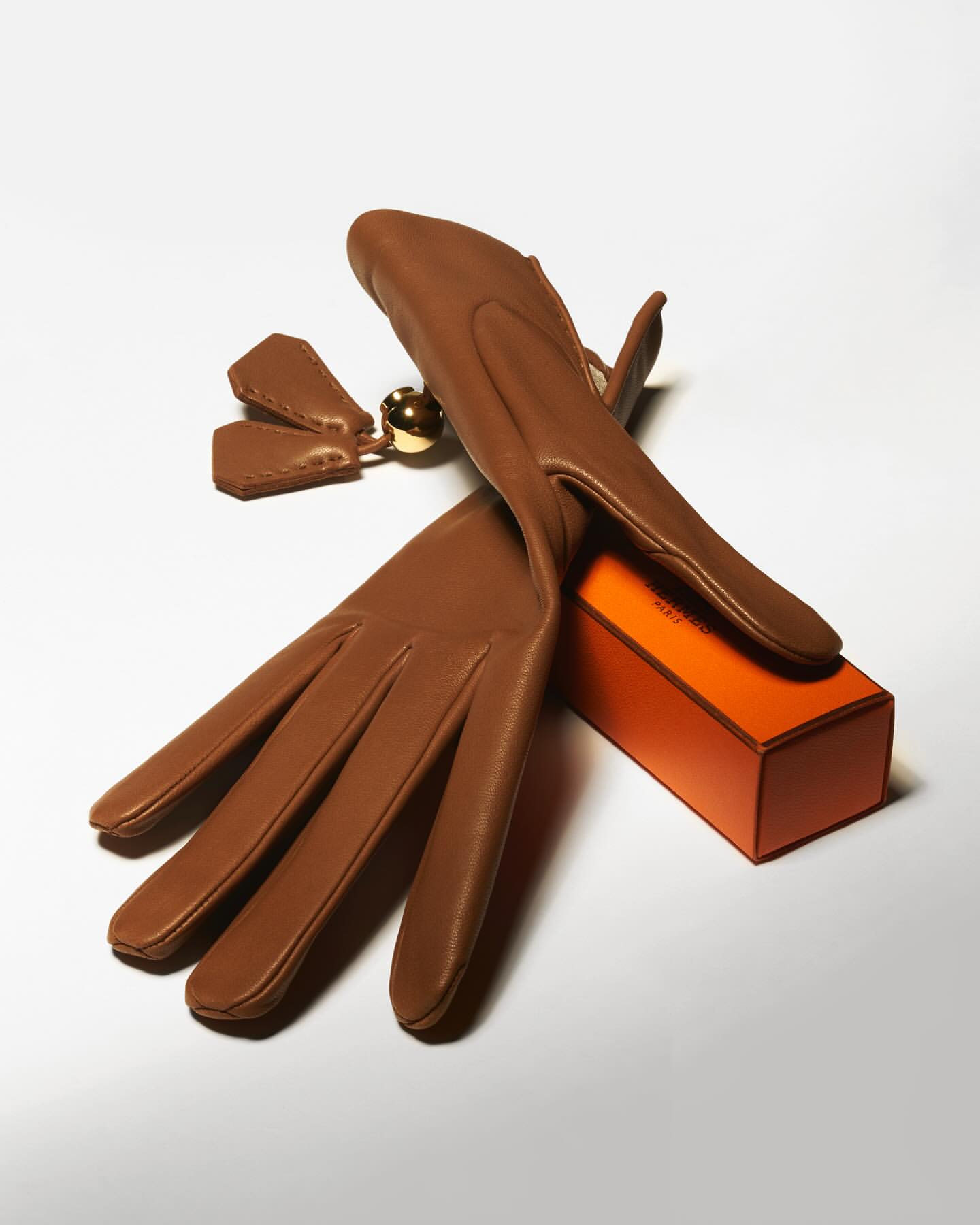 Pair of caramel-colored leather gloves arranged next to a small orange box, creating a minimalist and fashion-forward still life.