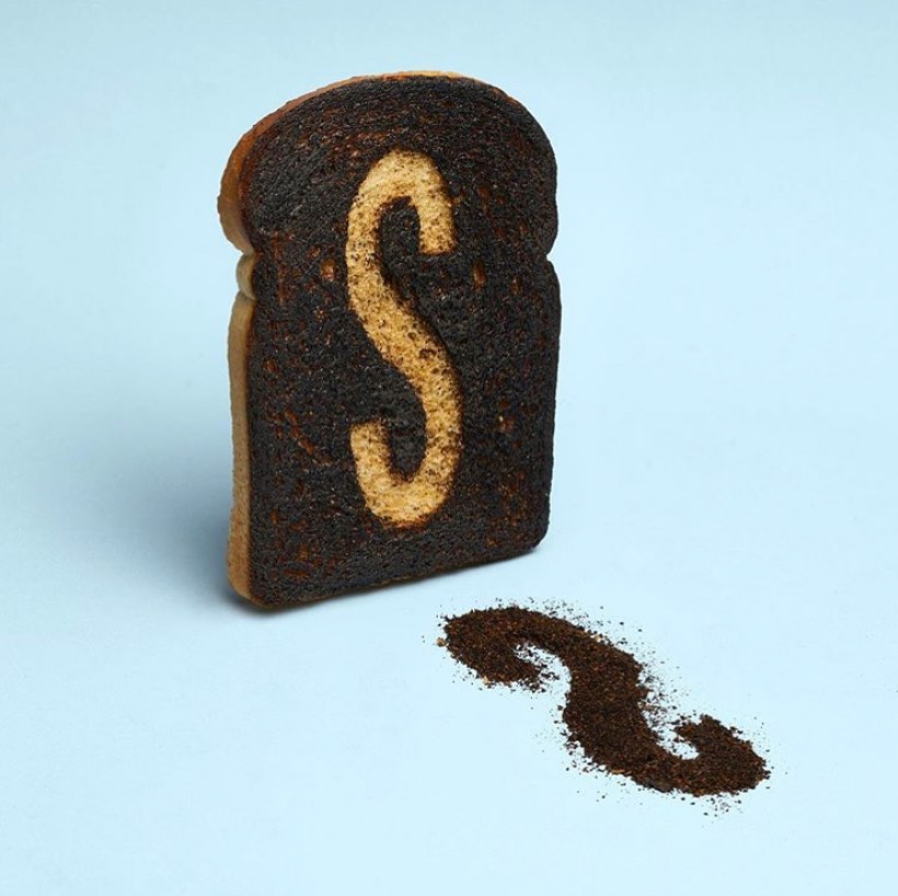 Burnt toast slice with an 'S' cutout on a pale blue background, accompanied by crumbs shaped like 'S' on the surface.
