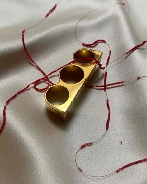 Close-up of a gold multi-finger ring resting on smooth white fabric intertwined with delicate red threads.