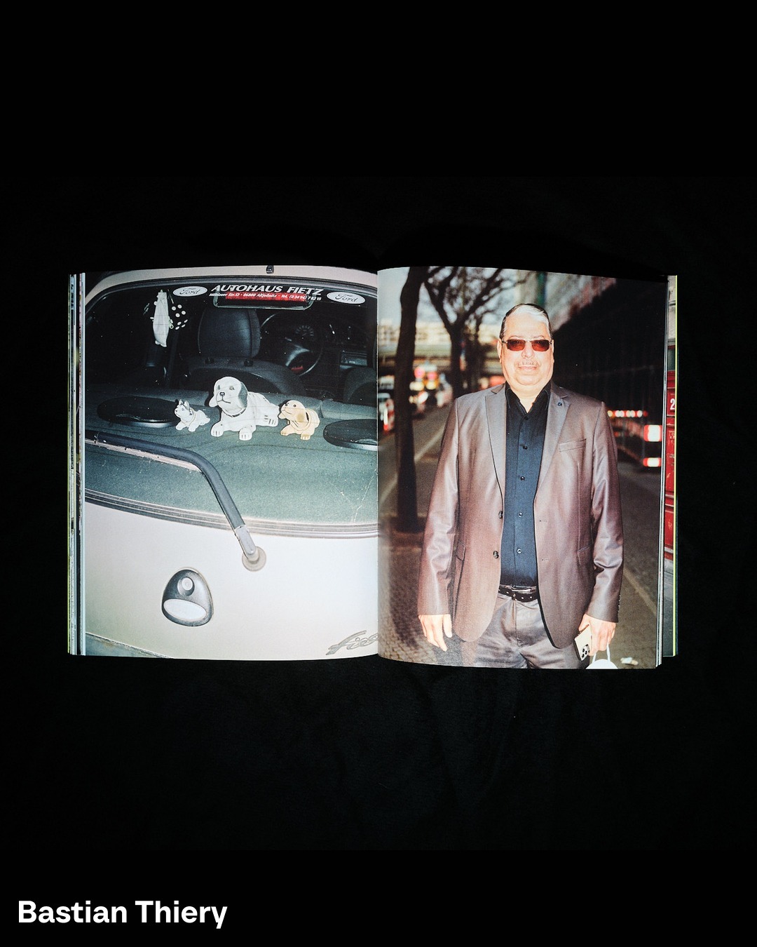 Open magazine spread showing a man in a suit on the right and a car interior with dog figurines on the left page.