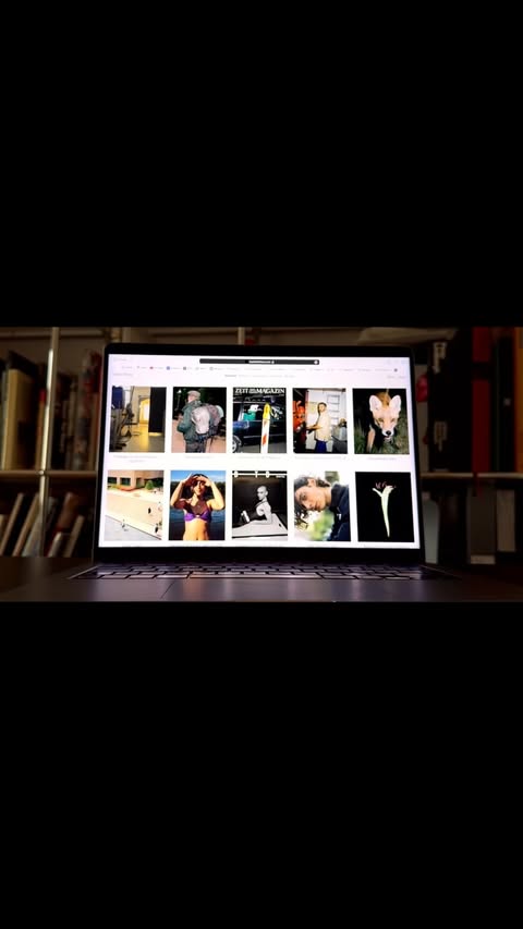 Open laptop displaying images on a wooden desk in front of a bookshelf, focusing on digital content viewing at home.