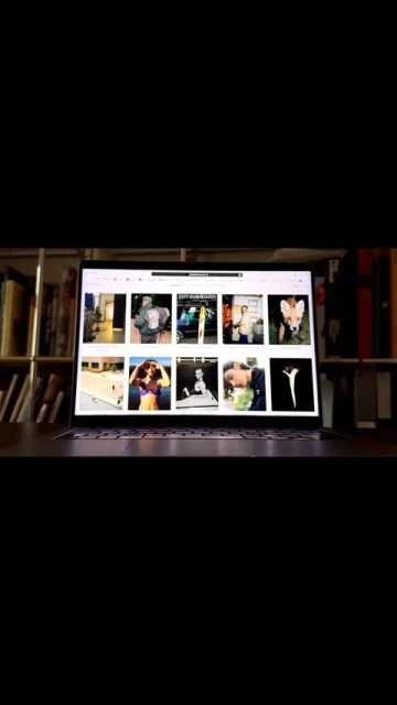 Open laptop displaying images on a wooden desk in front of a bookshelf, focusing on digital content viewing at home.