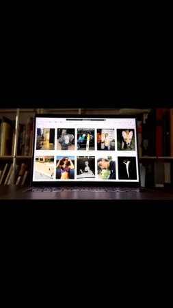 Open laptop displaying images on a wooden desk in front of a bookshelf, focusing on digital content viewing at home.