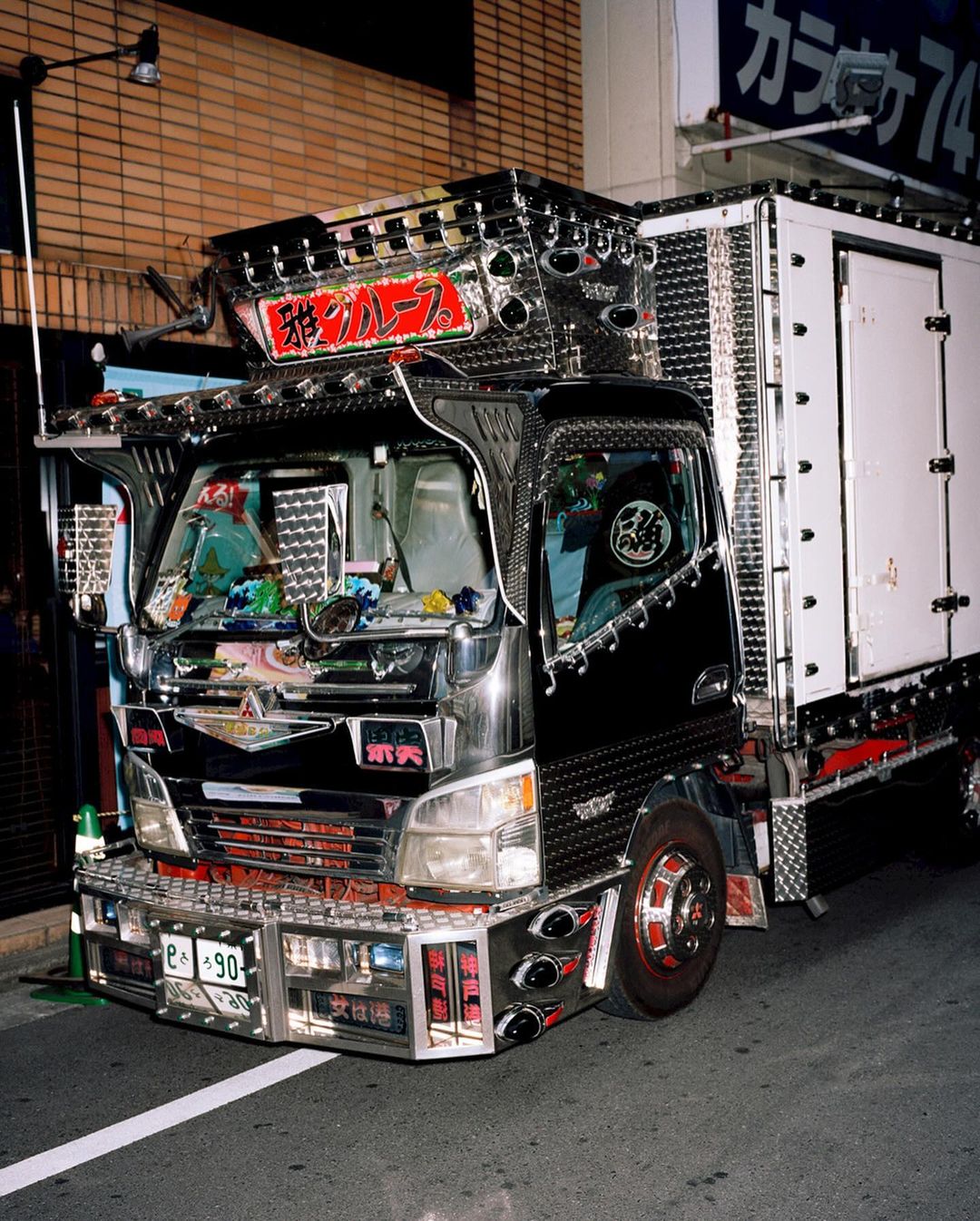 Decorated box truck with chrome accents parked on a city street at night, featuring Japanese text and neon lighting.