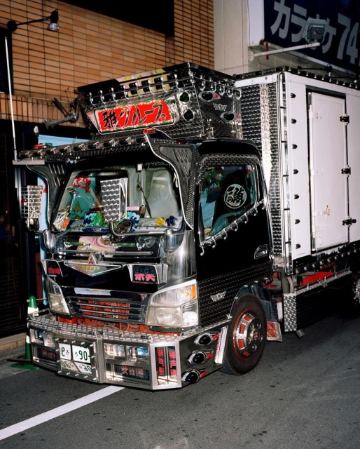 Decorated box truck with chrome accents parked on a city street at night, featuring Japanese text and neon lighting.
