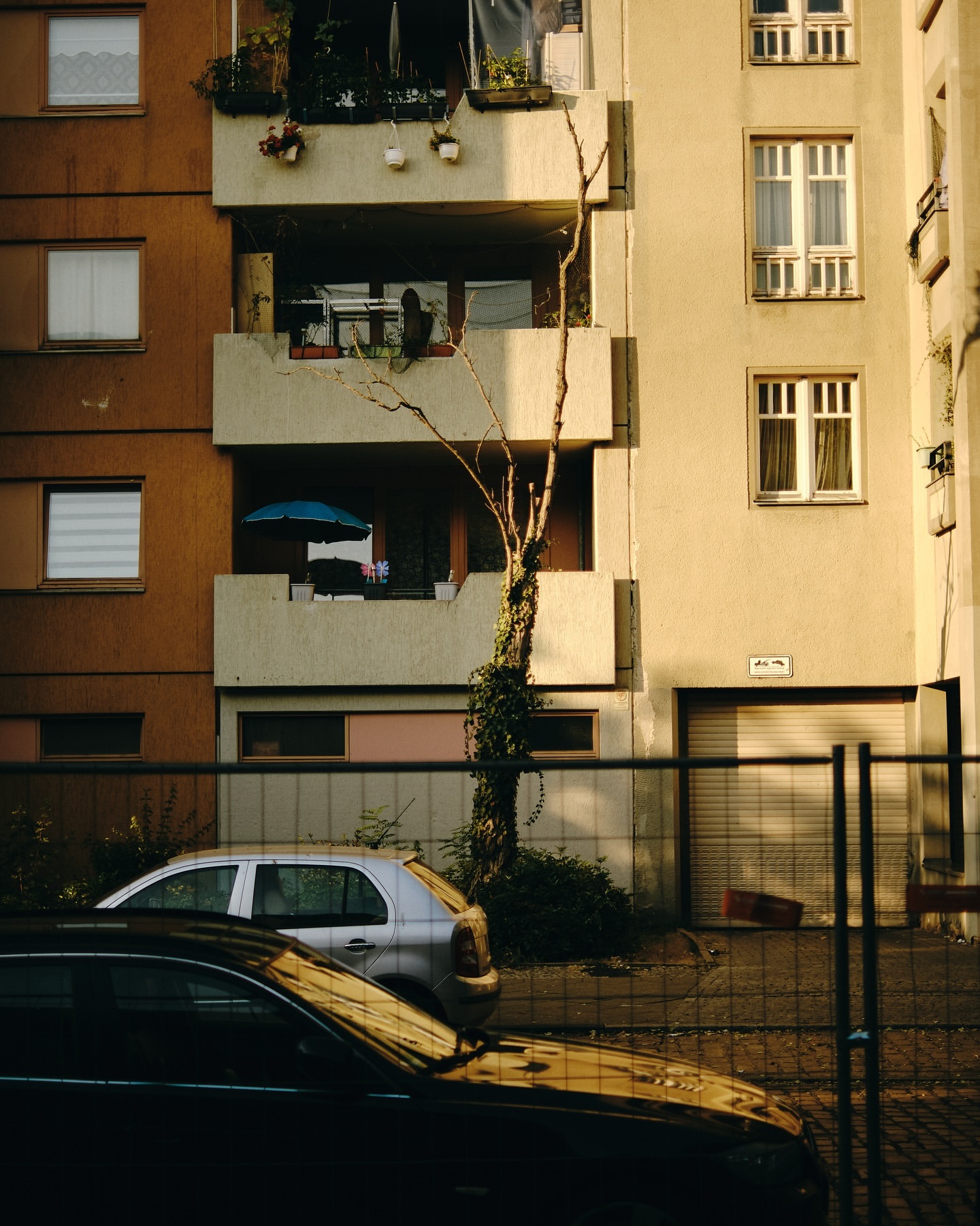 Exterior daytime view of a multi-story apartment building with balconies, windows, and cars parked on the street in front.