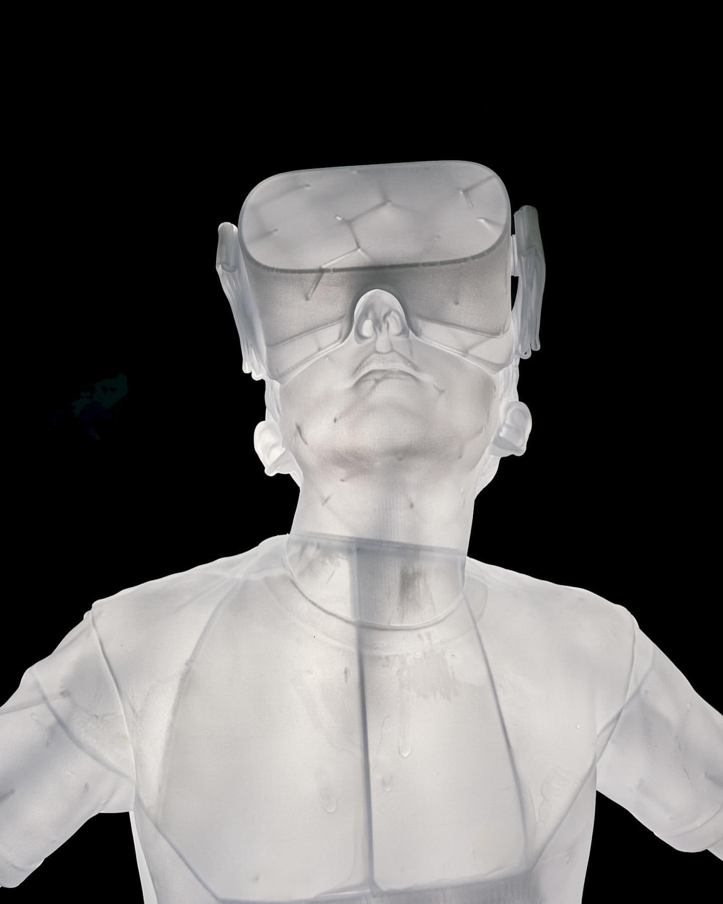 Translucent human bust wears a VR headset against black. The white sculpture is set against a stark, dark backdrop.