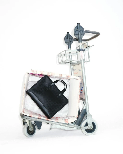 Black briefcase on a metal luggage cart filled with packing materials and covered in text patterns, set against a white background.
