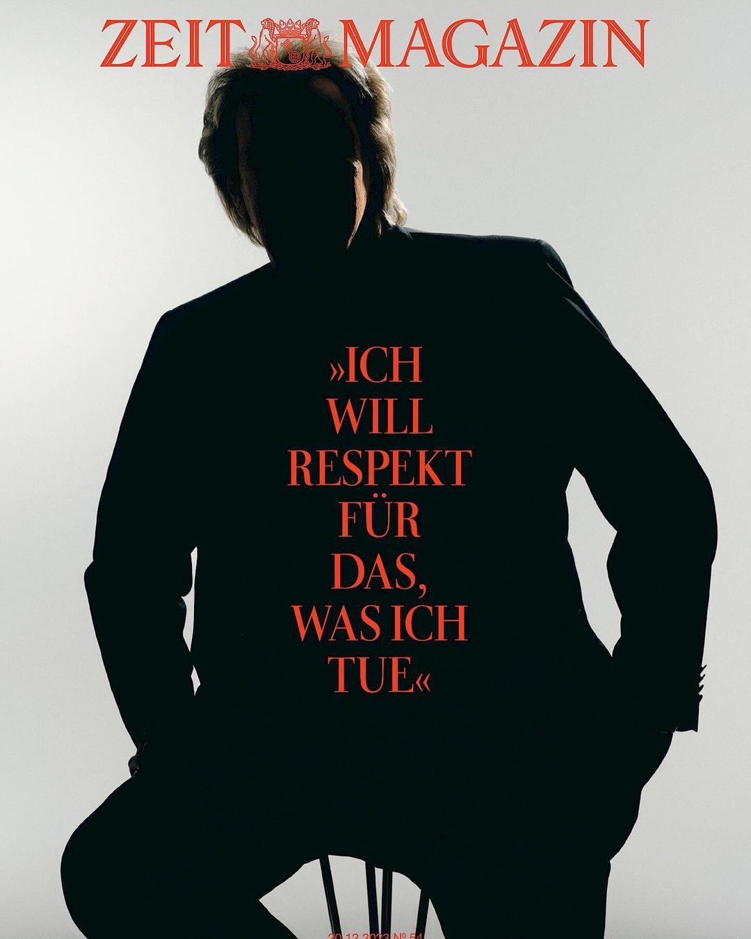 Silhouette of a man seated against a bright white background with large red magazine typography across his jacket.