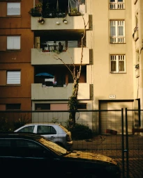 Apartment building exterior in Berlin with balconies, parked cars, and a bare tree photographed by Bastian Thiery