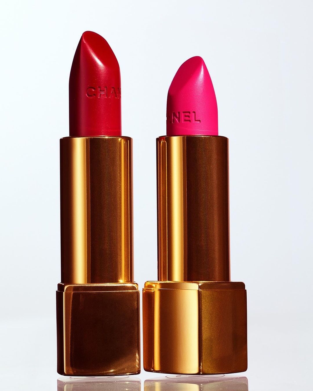 Two vibrant Chanel lipsticks in red and pink, displayed against a soft gradient background, showcasing luxury makeup and beauty aesthetics.